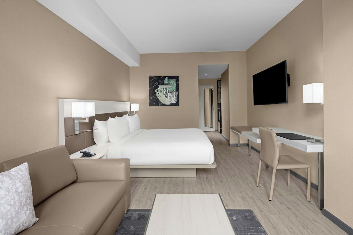 Ein modernes Hotelzimmer mit Bett, Schreibtisch, Stuhl, Fernseher und einem Bild an der Wand.