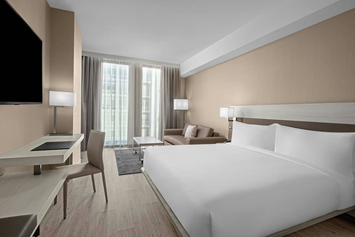 Ein Hotelzimmer mit einem großen Bett, einem Schreibtisch, einem Sessel, zwei Lampen und einem Fernseher.