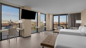 Une chambre d’hôtel dotée d’une grande fenêtre, d’un téléviseur à écran plat, d’un bureau, d’une chaise, d’un lit et d’un canapé.