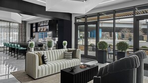 Un hall d’entrée moderne comprenant un canapé, des fauteuils, une table basse et un coin bar avec des étagères.