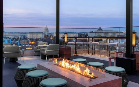 A rooftop bar with a fire feature, seating, and a view of the Capitol.