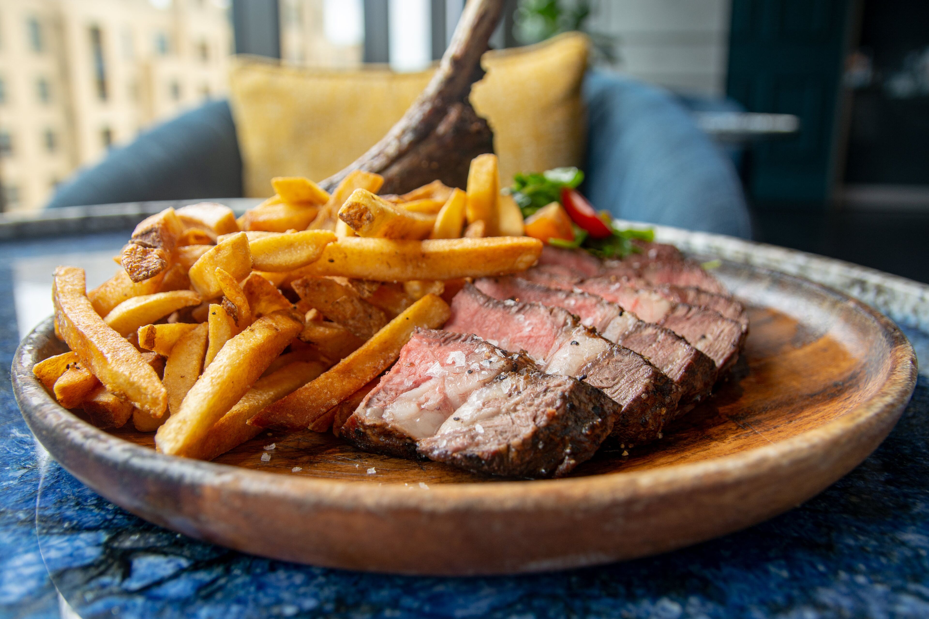 Une assiette de steak et de frites sur une table en bois, avec une vue sur la ville en arrière-plan.