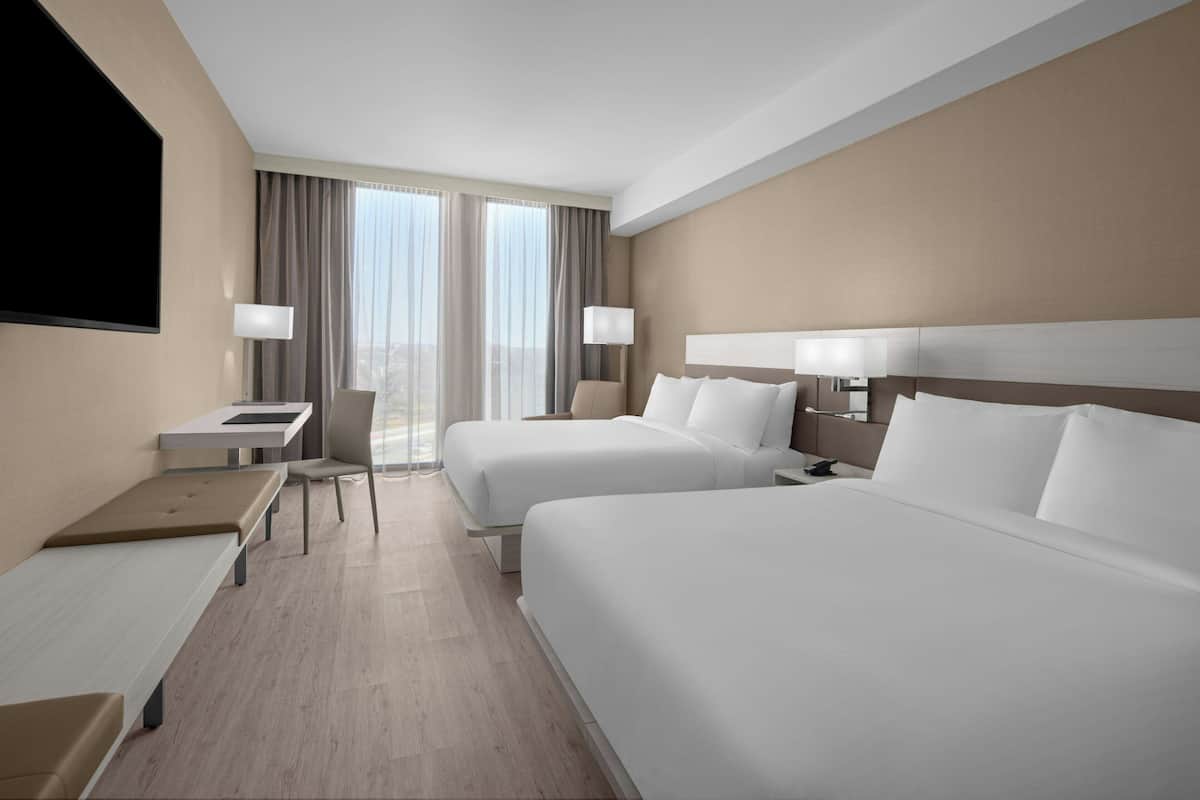 Ein Hotelzimmer mit zwei Betten, einem Schreibtisch, einem Stuhl und einem Fernseher.