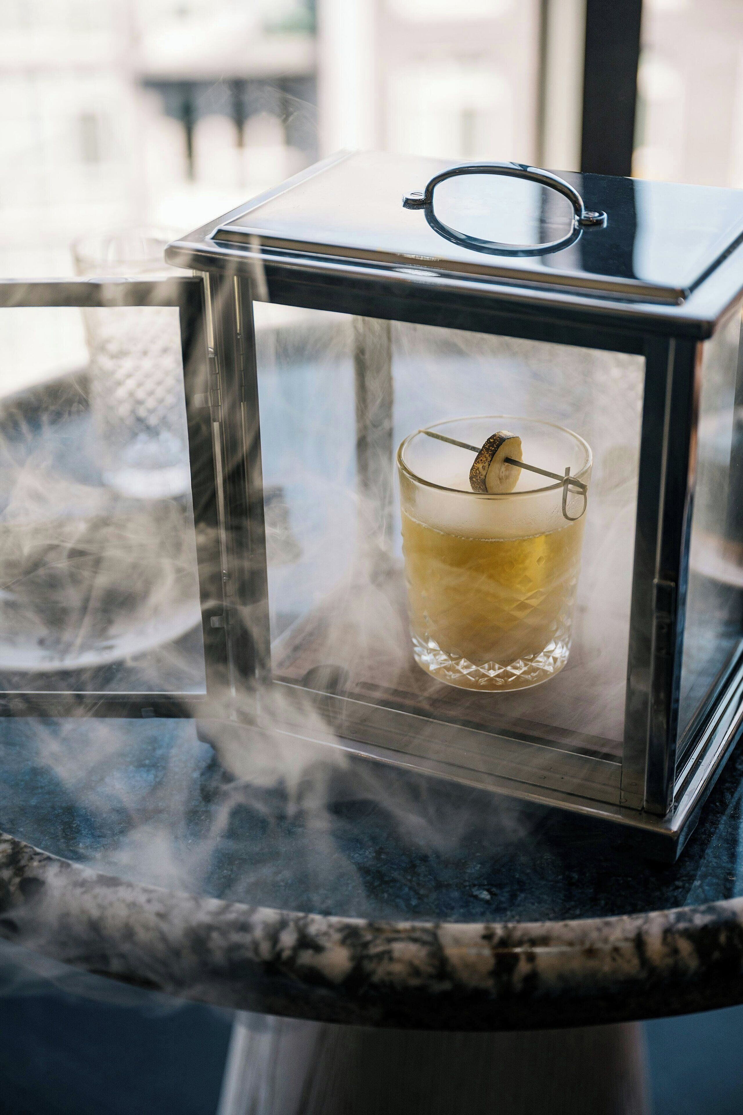 Un vaso de una bebida transparente con una rodaja de limón sobre una mesa con estructura de vidrio.