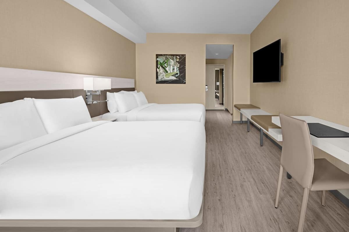 Ein Hotelzimmer mit zwei Betten, einem Schreibtisch, einem Stuhl, einem Fernseher und einem Bild an der Wand.