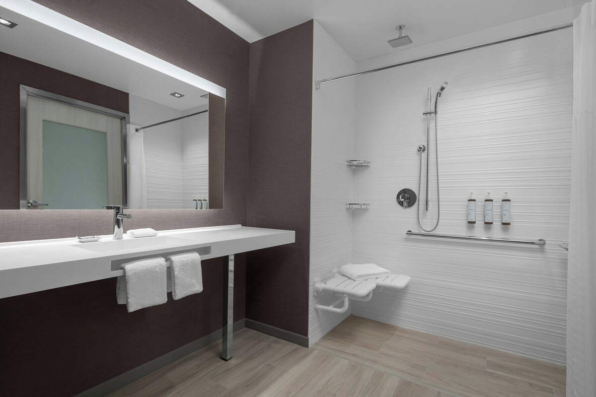 Une salle de bain moderne avec un grand miroir, un lavabo blanc, une douche avec une porte en verre et un porte-serviettes.