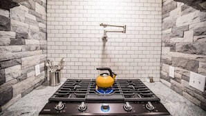 A kitchen with a gas stove, a kettle, and a stone wall backsplash. - THE FAMILY FOREST · ★3 Acres Of Forest★Lighted Yard★Chef Kitchen★ (Colorado Springs)