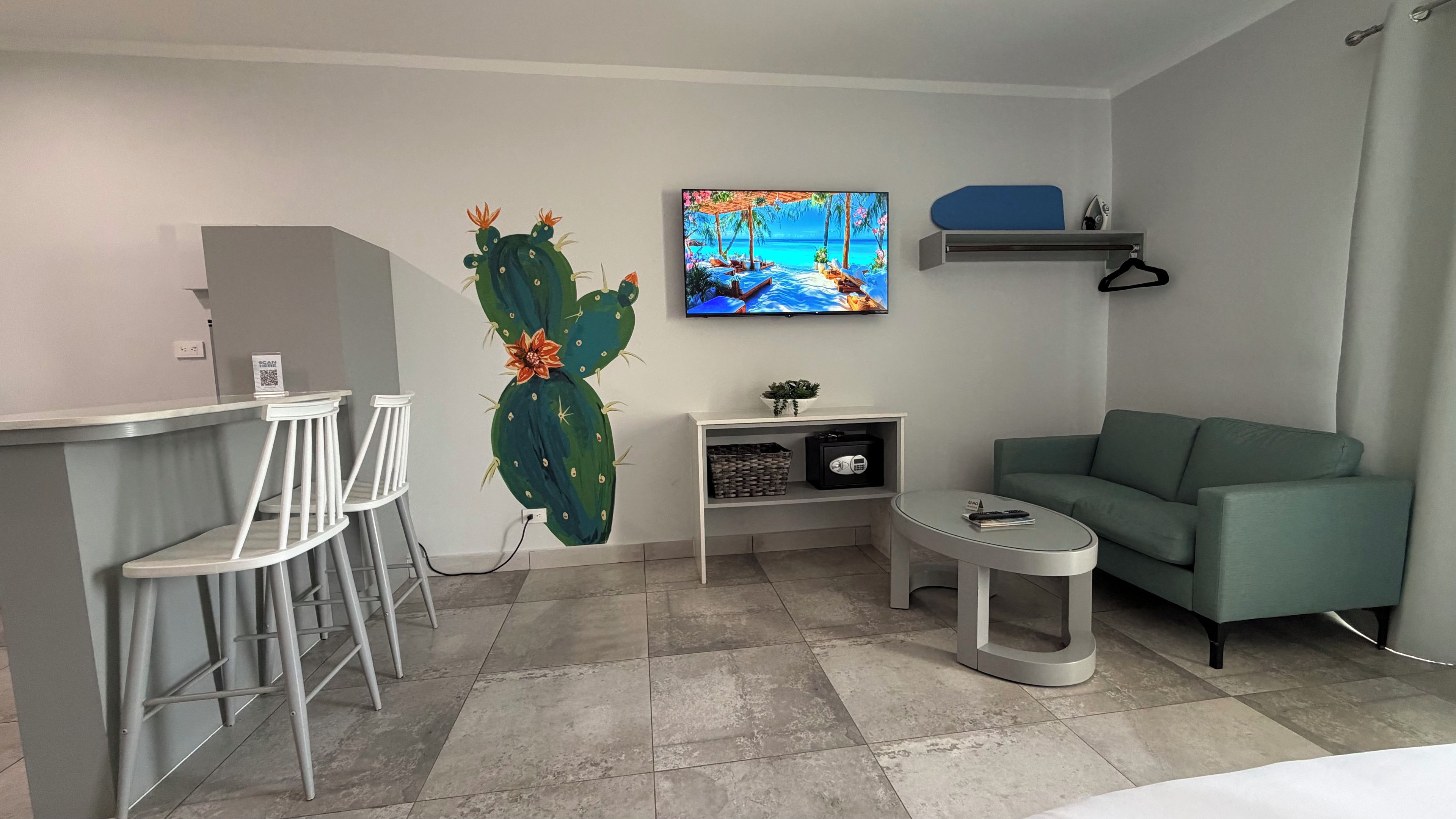 Una habitación moderna con barra, un sofá verde, una obra de arte con cactus y un televisor mostrando una escena de playa.