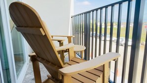 A wooden Adirondack chair on a balcony with a metal railing, a glass door, and a view of a parking lot. - Bushiri's Long Life Studio w/Kingbed & Balcony #5 (Oranjestad)