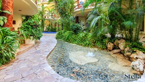 Un giardino tropicale con un vialetto acciottolato, vegetazione lussureggiante e un elemento d'acqua.