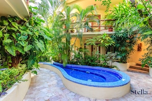 A pool with a curved edge, surrounded by lush greenery and a tiled floor.