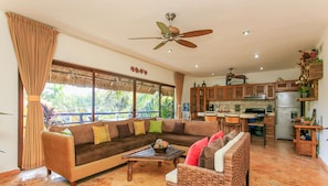 Relax in this spacious living area with a comfortable sofa set and coffee table, offering a view of lush greenery outside.