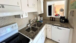 Una cucina compatta con mobili bianchi, un piano di lavoro in granito, lavastoviglie integrata e una finestra con vista.