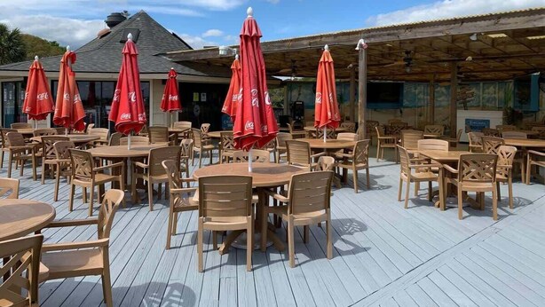 Un'area patio esterna con tavoli e sedie in legno, ombrelloni rossi e una struttura con tetto in legno.