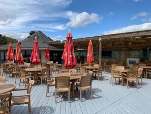 Ein Außenbereich mit einer Terrasse, Holztafeln und -stühlen, roten Sonnenschirmen und einem Holzdach.