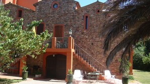 A stone building with a staircase leading to a balcony, outdoor seating, and potted plants. - Le Marronnier à la Bouverie (ROQUEBRUNE SUR ARGENS)