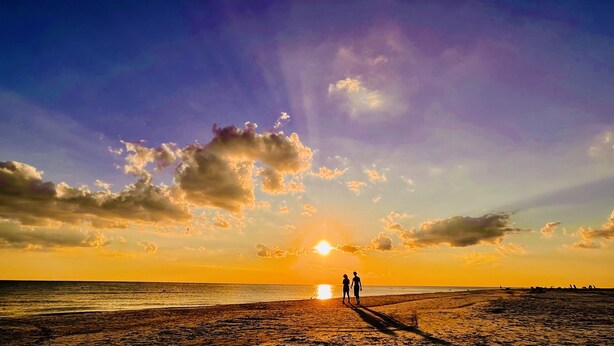 A beach scene with two people silhouetted against a sunset.
