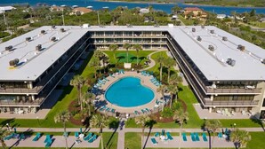 A hotel with a central swimming pool, multiple balconies, and a view of the surrounding landscape.