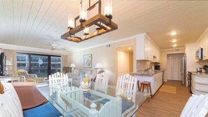 A spacious living area with a glass dining table, white chairs, and a modern chandelier.