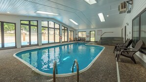 Ein Innenpool mit großen Glaswänden, Fliesenboden und einigen Liegestühlen.