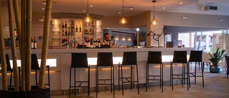 Zona de bar con mostrador, varios taburetes y una variedad de botellas y vasos.