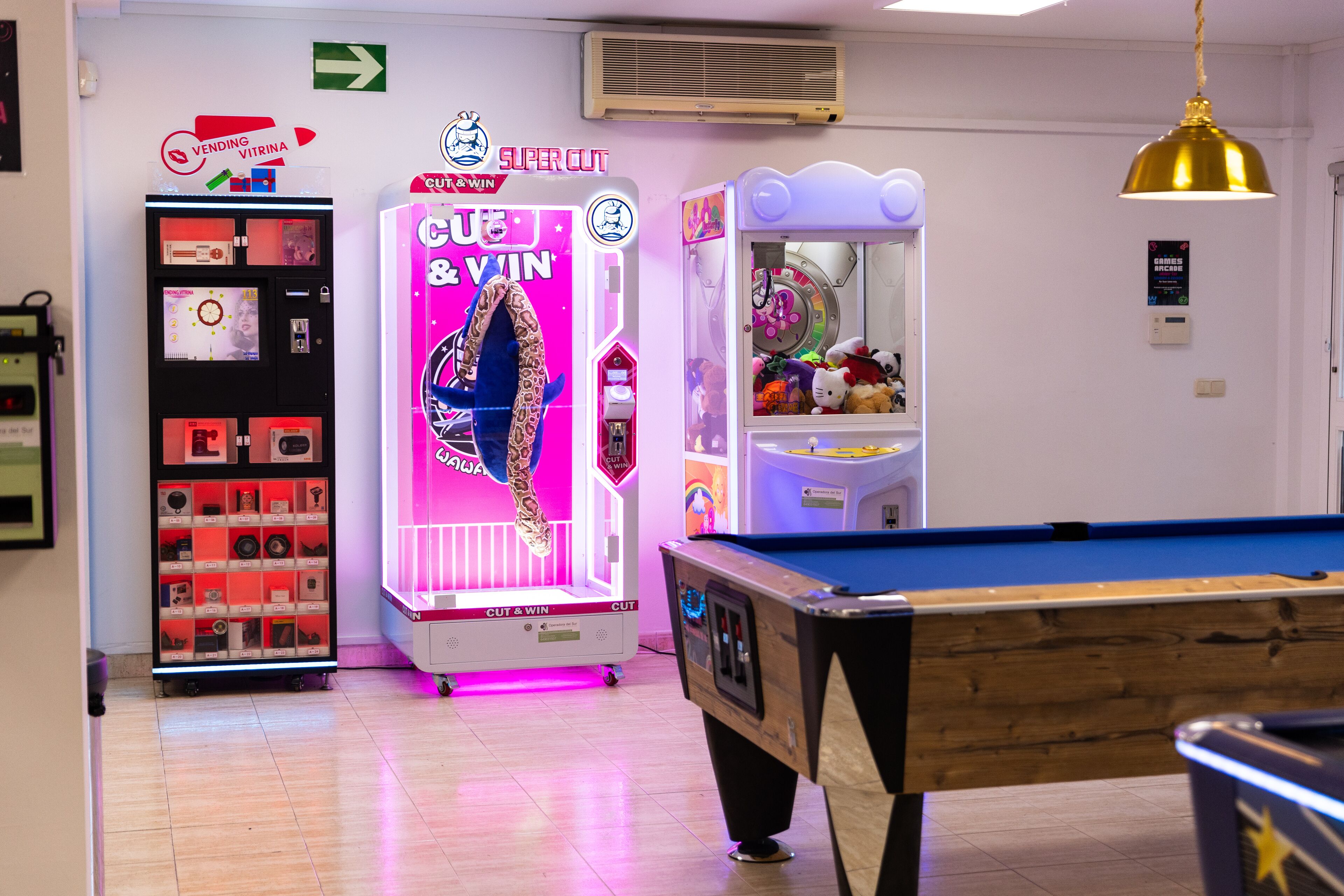 A room with a pool table, a vending machine, and a claw machine.