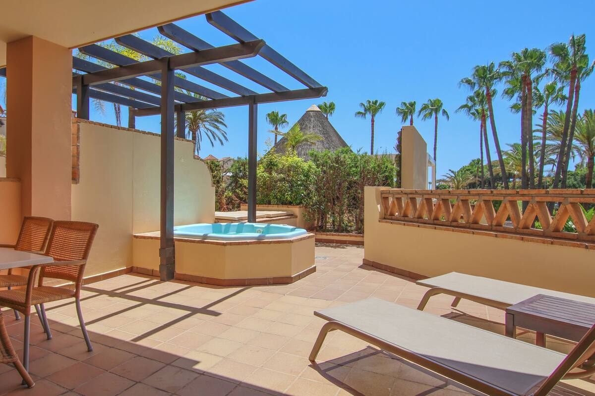 An outdoor patio with a hot tub, lounge chairs, and a pergola.