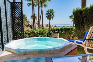 A hot tub with a view of the sea, surrounded by palm trees and a poolside area with lounge chairs.