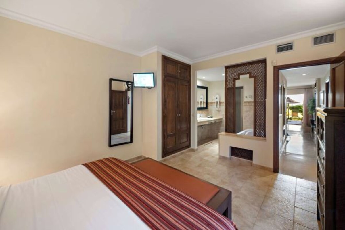 Habitación de hotel con cama, televisión, baño y pasillo que da a otras habitaciones.