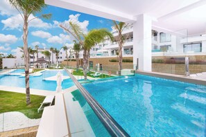 A modern hotel with a large swimming pool, palm trees, and a clear blue sky. - Wyndham Grand Costa del Sol (Mijas)