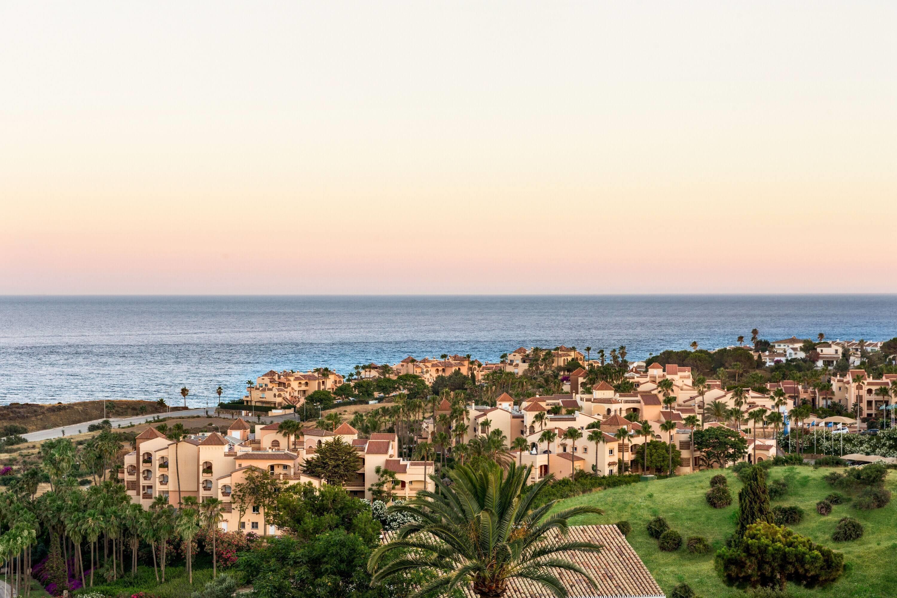 Ein Küstenwohngebiet mit mehreren Gebäuden, von denen einige Balkone haben, und Blick auf das Meer.