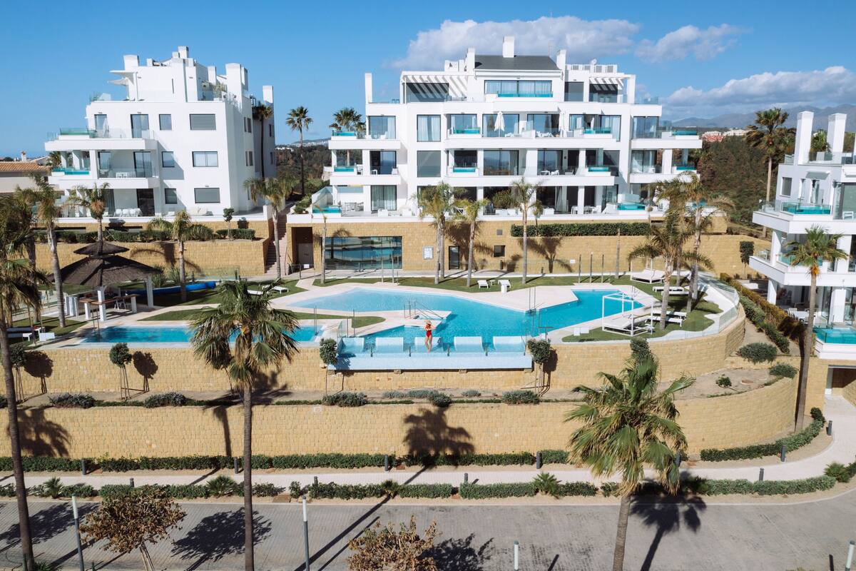 A modern resort with a central pool, multiple balconies, and palm trees.