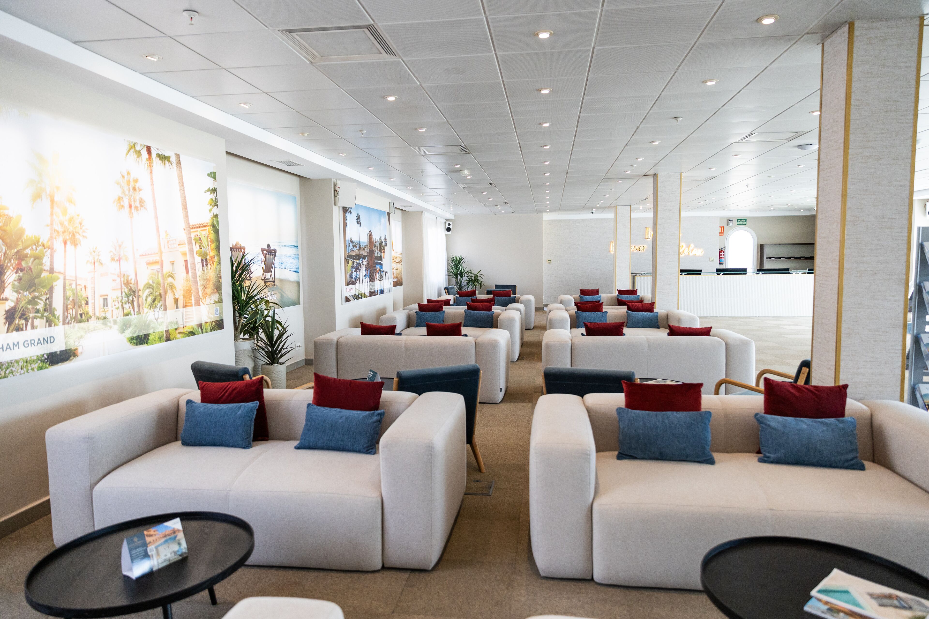 A modern hotel lobby with white sofas, red and blue cushions, and black coffee tables.