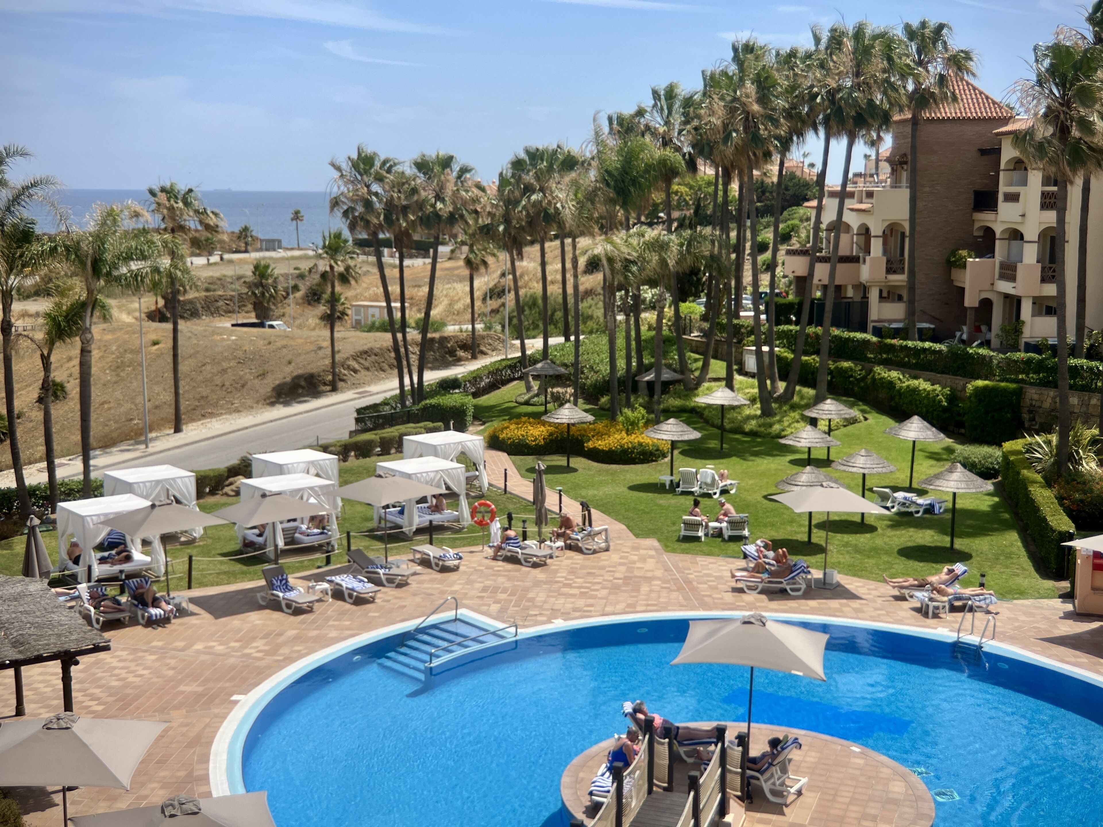 A resort with a pool, lounge chairs, umbrellas, and palm trees.