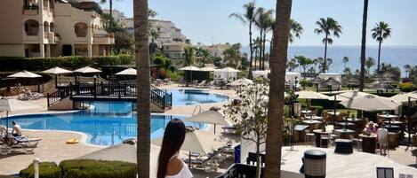 A resort with a swimming pool, lounge chairs, umbrellas, and a view of the ocean.