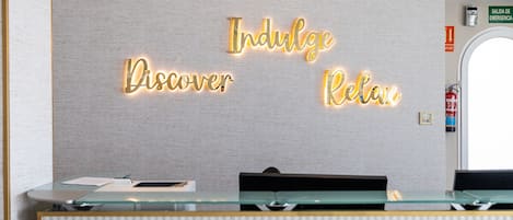 Un mostrador de recepción con un letrero iluminado que dice "Indulge Discover Relax".