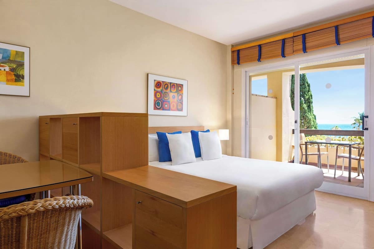 A hotel room with a bed, a desk, a chair, and a balcony with a view.