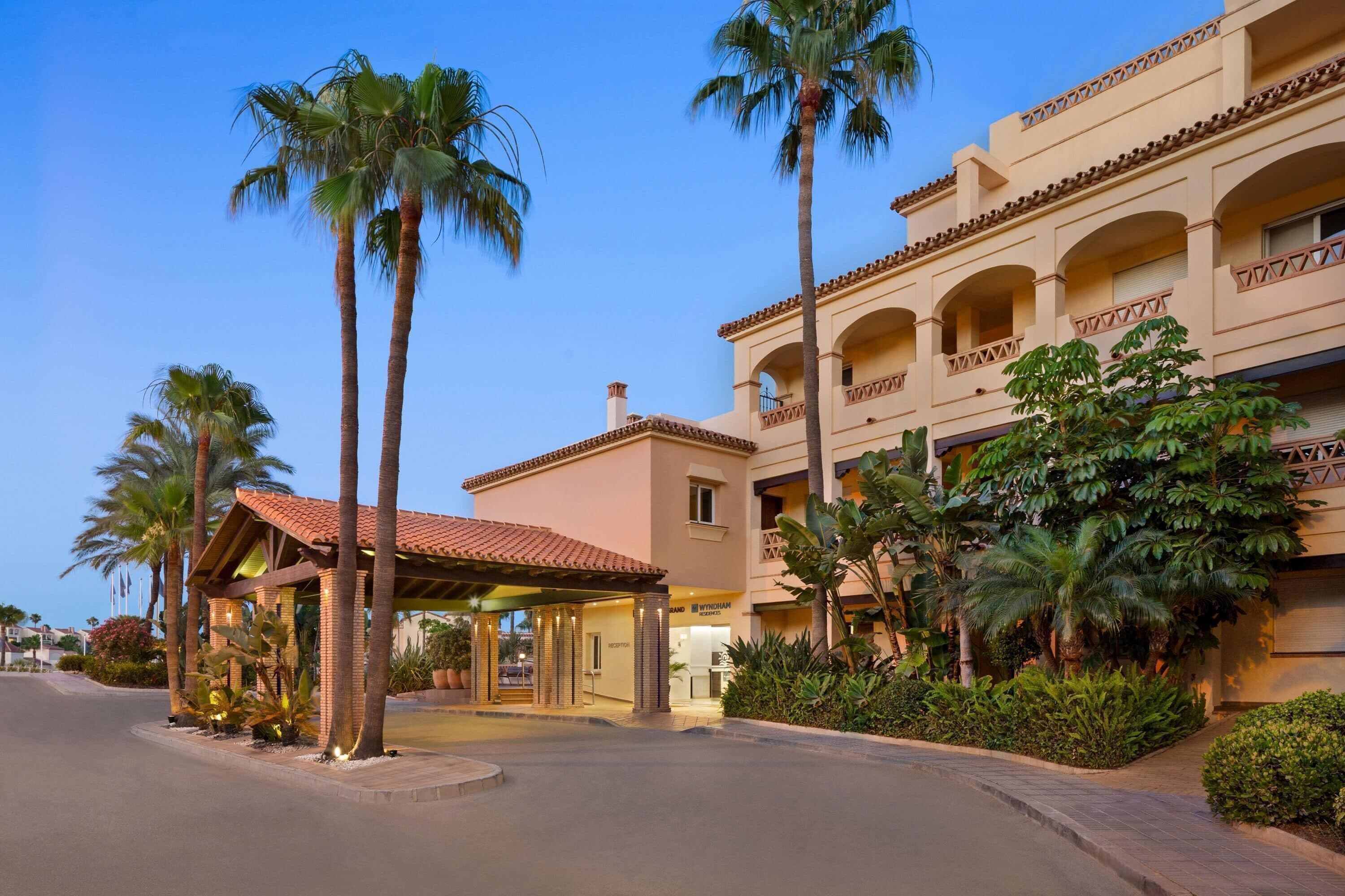 A hotel with a reception area, palm trees, and a building with balconies.