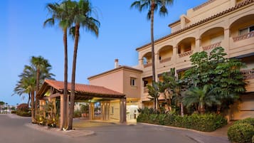 Un hotel con una zona de recepción, palmeras y un edificio con balcones.