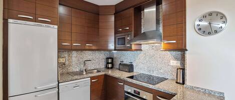 A modern kitchen with wooden cabinets, stainless steel appliances, granite countertops, and a wall clock.