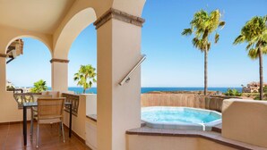 Un balcón con jacuzzi, sillas y vista al mar.