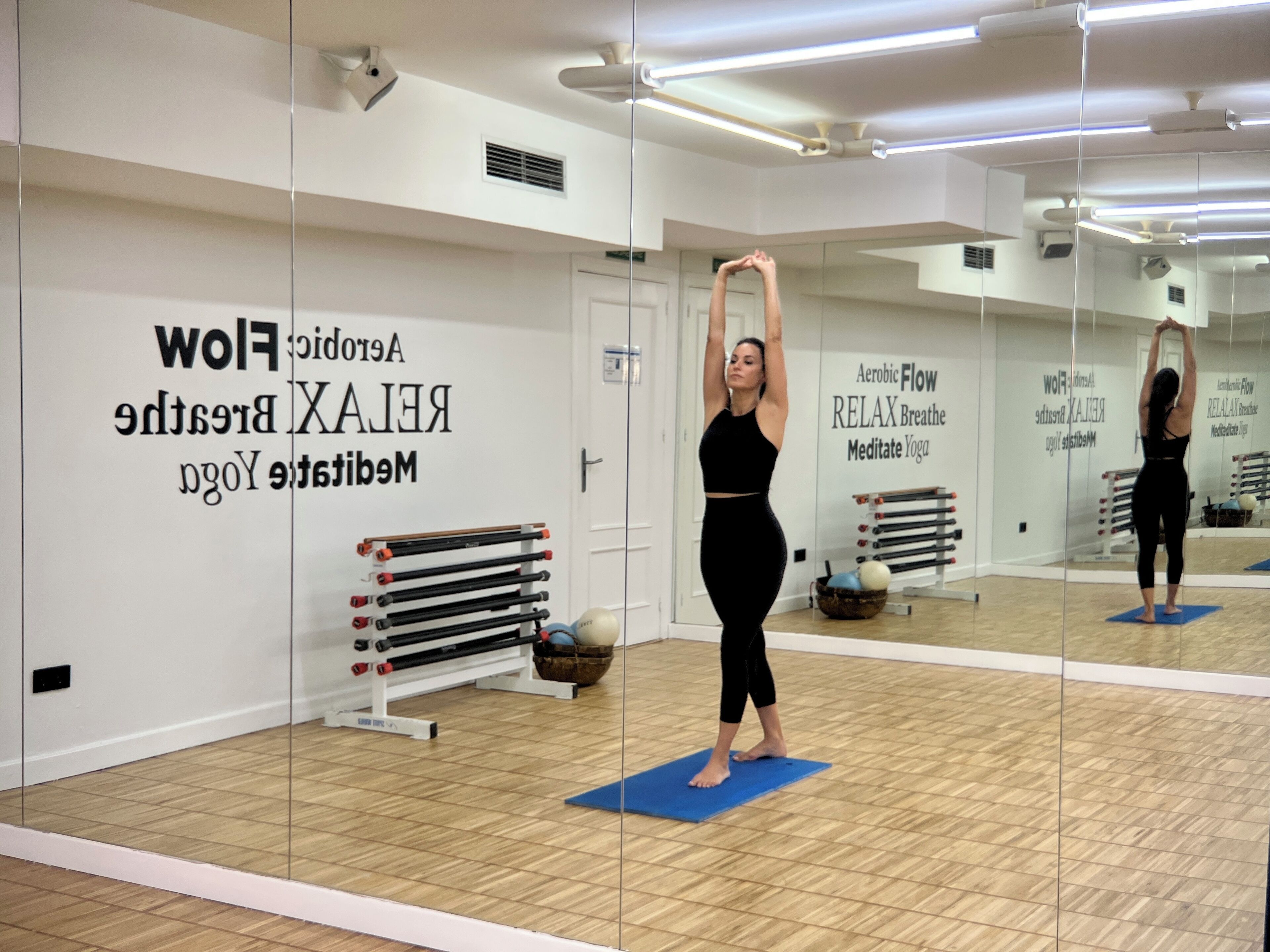 A yoga studio with mirrored walls, a wooden floor, and exercise equipment.