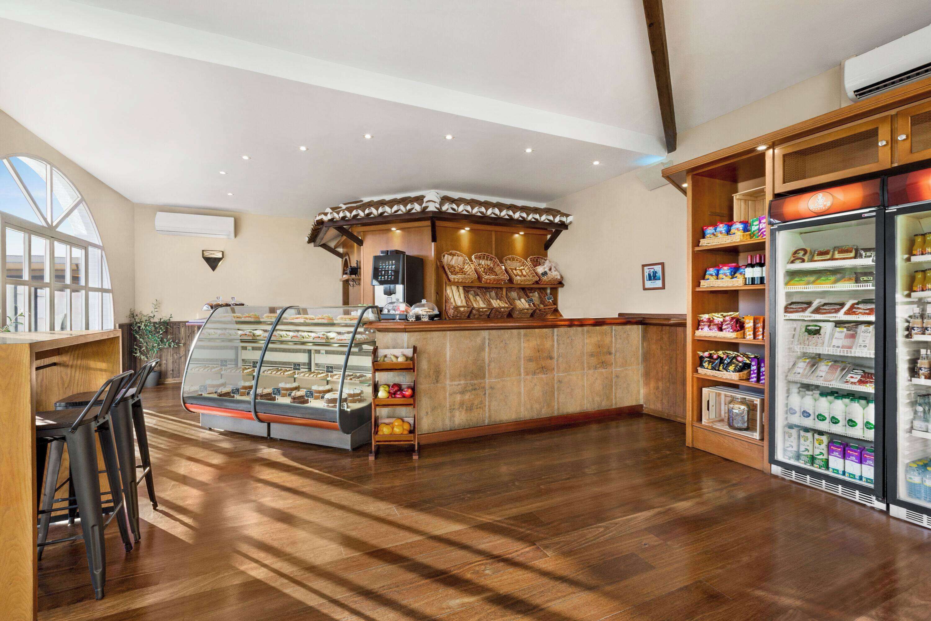 A bakery counter with a display case, wooden bar stools, and a refrigerated display with various products.