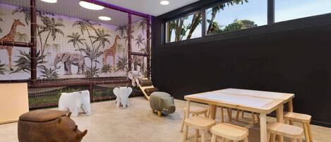A room with a large window, a table with chairs, a sofa, and a mural of animals on the wall.