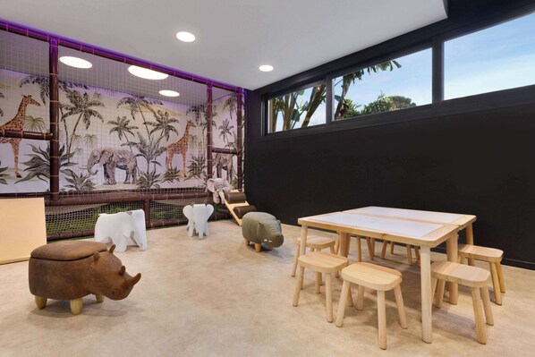 A room with a large window, a table with chairs, a sofa, and a mural of animals on the wall. - Wyndham Grand Costa del Sol (Mijas)