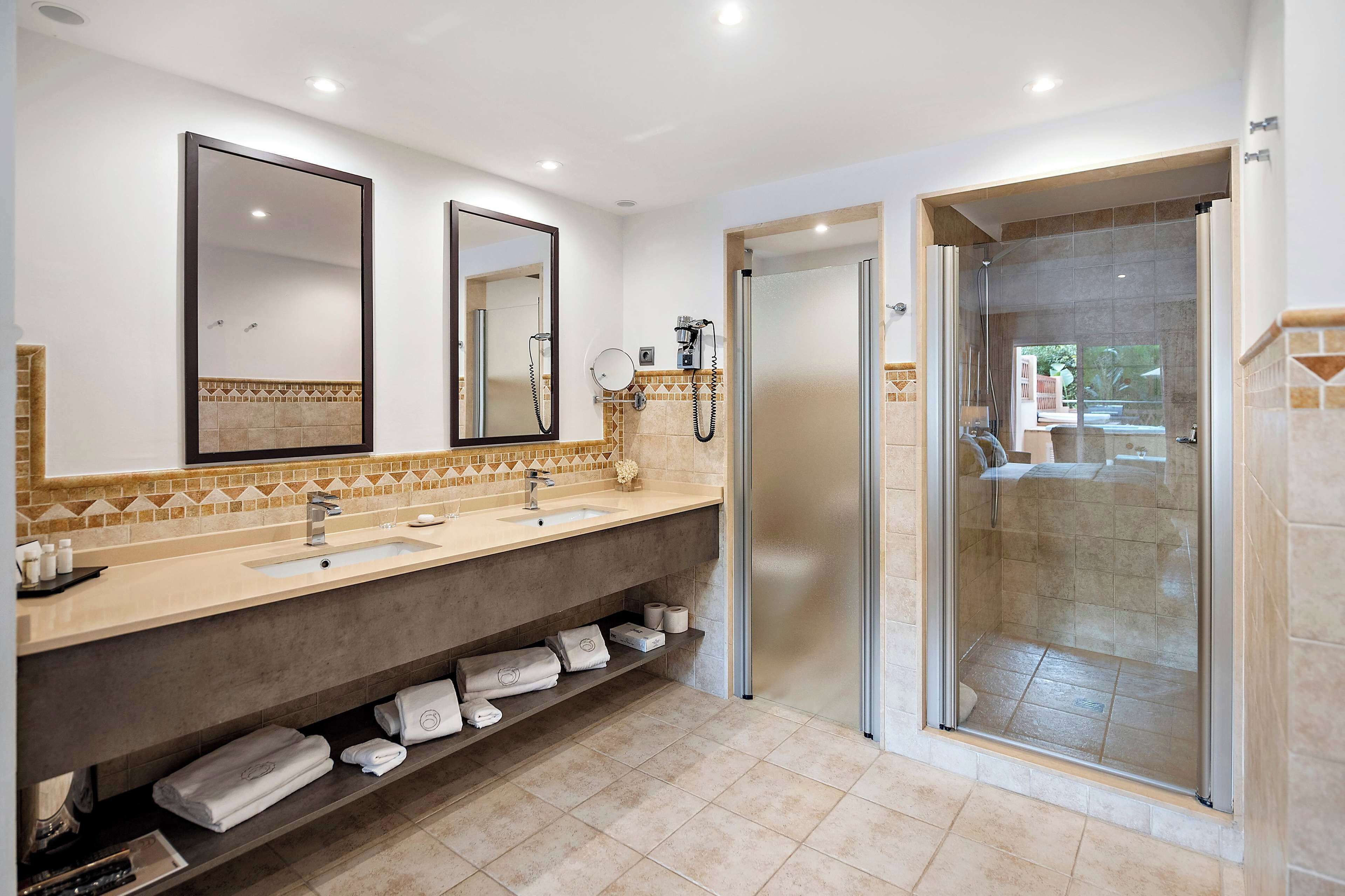 Een moderne badkamer met twee wasbakken, een grote spiegel, een douchecabine en een handdoekrek.