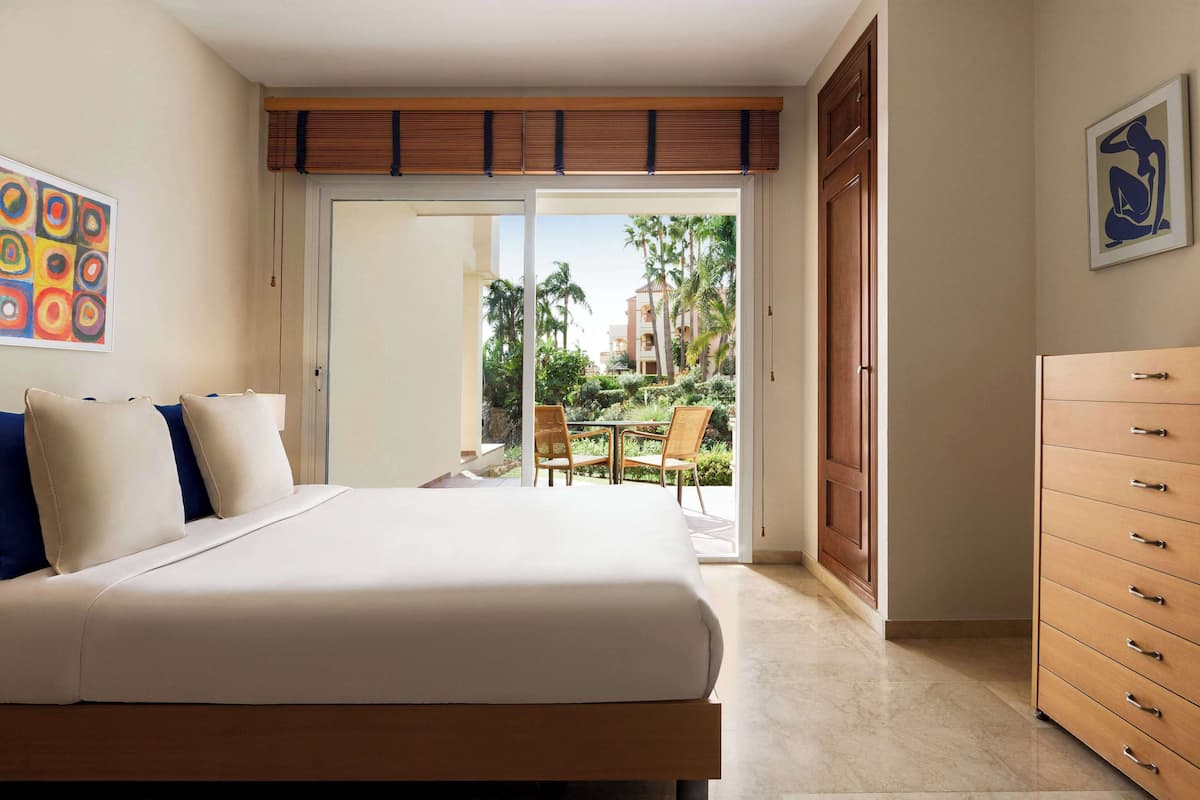 A hotel room with a large bed, a wooden dresser, and a view of a patio with outdoor furniture.