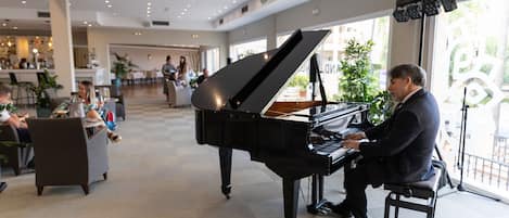 Un piano de cola imponente en un vestíbulo amplio y bien iluminado, con una decoración moderna y ventanas grandes.