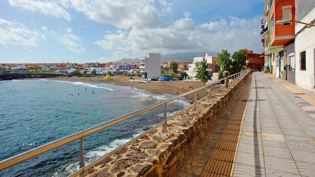 Un paseo marítimo con un muro de piedra, barandilla metálica y edificios con balcones.