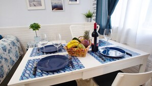 Una mesa de comedor dispuesta con platos, cubiertos, una botella de vino y una cesta de frutas.